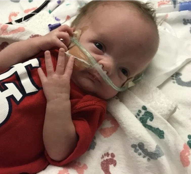 Gus, wrapped in a blanket and wearing a red top, with a nasal cannula